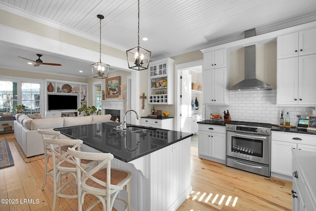 kitchen featuring wall chimney range hood, stainless steel gas stove, a kitchen island with sink, a kitchen breakfast bar, and decorative backsplash