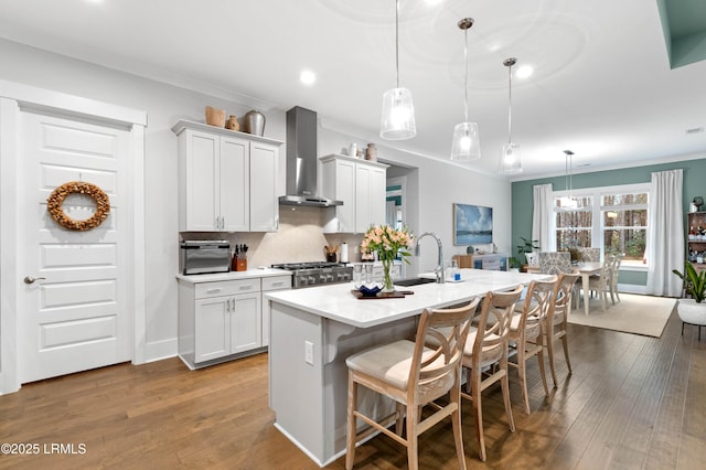 kitchen featuring pendant lighting, sink, a kitchen breakfast bar, a center island with sink, and wall chimney exhaust hood