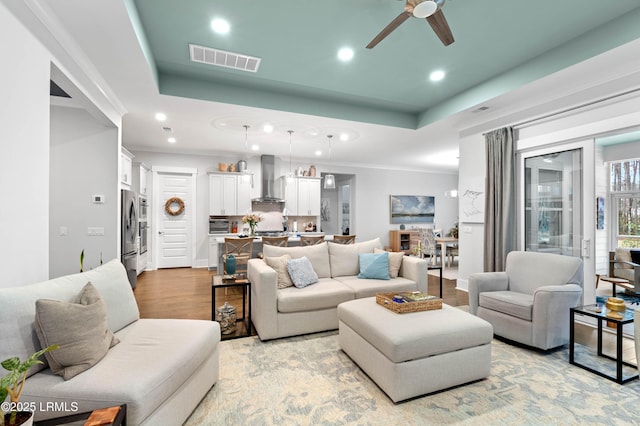 living room with a tray ceiling, light hardwood / wood-style flooring, ornamental molding, and ceiling fan