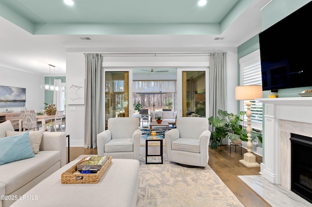 living room with a raised ceiling, a premium fireplace, hardwood / wood-style floors, and ceiling fan