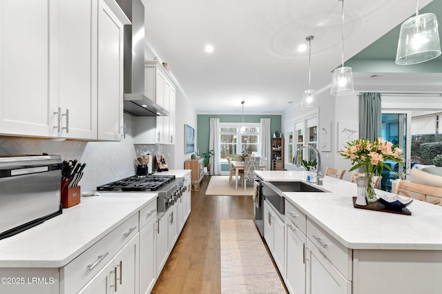 kitchen with wall chimney exhaust hood, sink, a kitchen island with sink, and hanging light fixtures