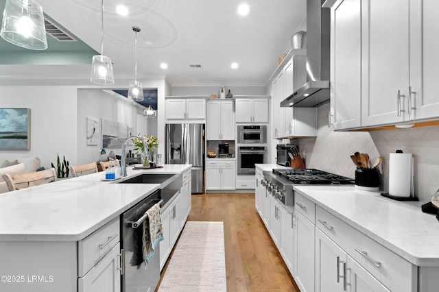 kitchen featuring decorative light fixtures, white cabinetry, a kitchen island with sink, stainless steel appliances, and wall chimney range hood