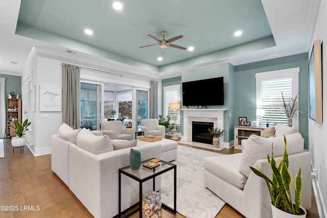 living room with light hardwood / wood-style flooring, ornamental molding, a raised ceiling, and plenty of natural light