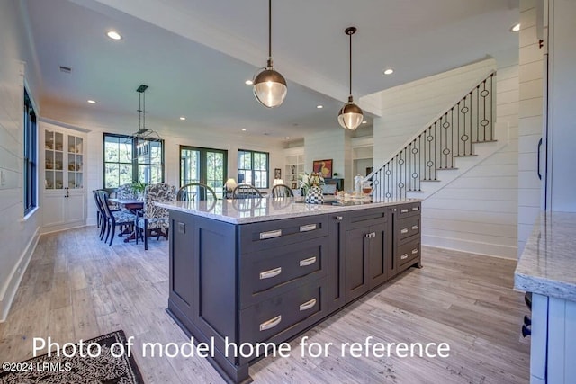 kitchen with light hardwood / wood-style flooring, pendant lighting, light stone counters, and a spacious island