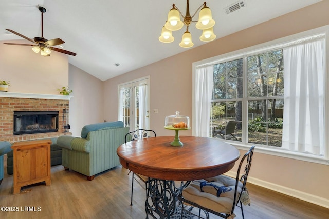 dining space with hardwood / wood-style flooring, lofted ceiling, a brick fireplace, and a healthy amount of sunlight