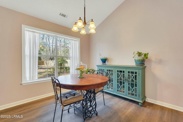 dining space with dark wood-type flooring, an inviting chandelier, and lofted ceiling