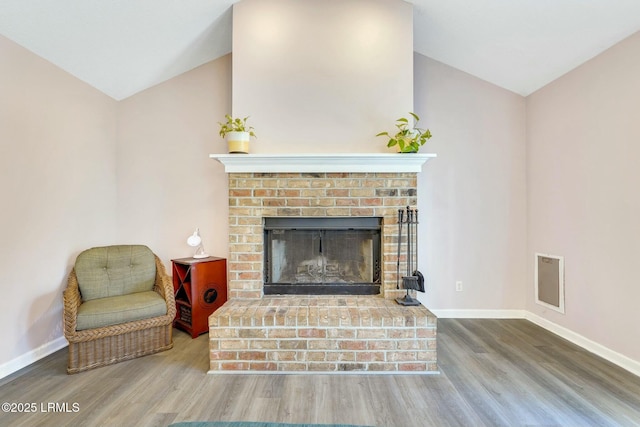 interior space featuring a brick fireplace, wood-type flooring, and lofted ceiling