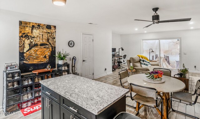 kitchen featuring light stone counters, ceiling fan, a center island, and light hardwood / wood-style floors