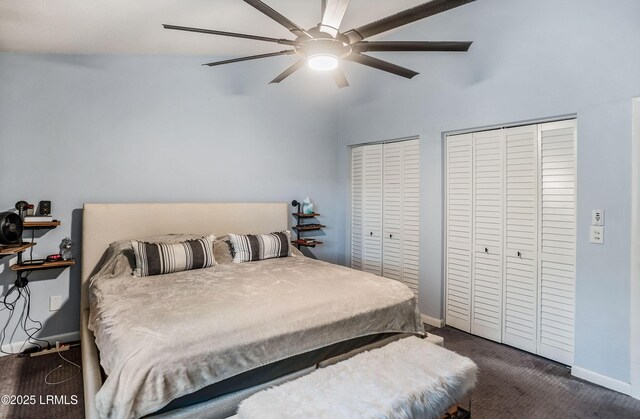 bedroom featuring ceiling fan, two closets, and dark colored carpet