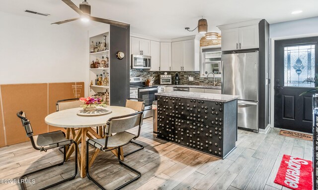 kitchen with tasteful backsplash, white cabinets, a center island, stainless steel appliances, and light stone countertops