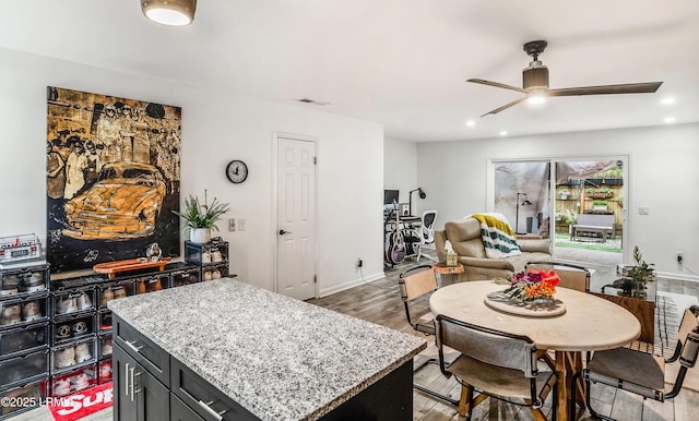 interior space with ceiling fan, a kitchen island, light wood-type flooring, and light stone counters