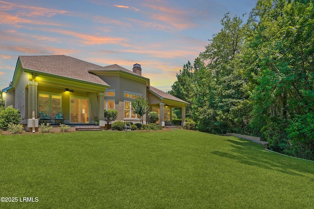 19 Lynnfield Pl, Bluffton, SC 29910 - back of house at dusk with a ceiling fan, a lawn, a chimney, and a shingled roof