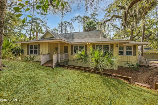 rear view of house featuring board and batten siding, a yard, and a shingled roof