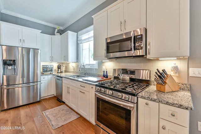 kitchen featuring sink, white cabinetry, light wood-type flooring, appliances with stainless steel finishes, and light stone countertops