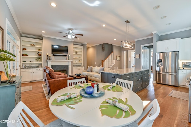 dining space featuring crown molding, light hardwood / wood-style flooring, built in features, and ceiling fan with notable chandelier