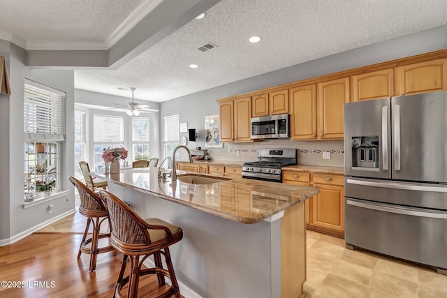 kitchen featuring backsplash, light stone countertops, a kitchen bar, appliances with stainless steel finishes, and a sink