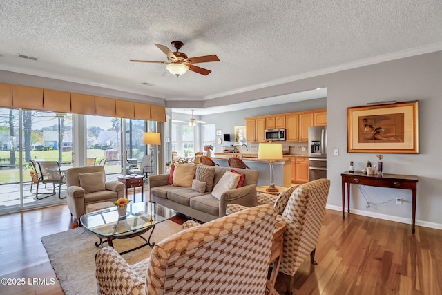 living area featuring visible vents, a ceiling fan, wood finished floors, crown molding, and baseboards