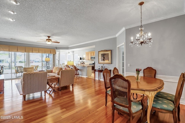 dining room with ceiling fan with notable chandelier, a textured ceiling, crown molding, and light wood finished floors