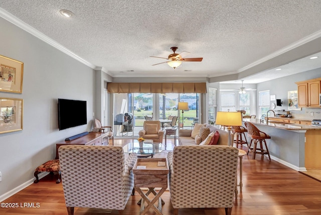 living area featuring wood finished floors, baseboards, ceiling fan, a textured ceiling, and crown molding