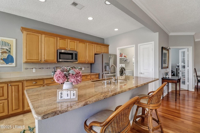 kitchen with visible vents, a sink, a kitchen breakfast bar, stainless steel appliances, and light stone countertops