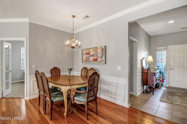 dining area featuring visible vents, a wainscoted wall, wood finished floors, a notable chandelier, and a textured ceiling