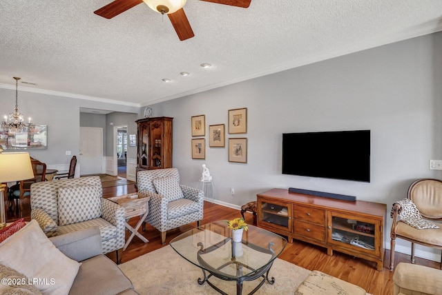 living room with ceiling fan with notable chandelier, a textured ceiling, wood finished floors, crown molding, and baseboards