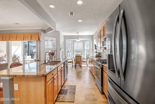 kitchen featuring a center island with sink, a sink, recessed lighting, stainless steel appliances, and light stone countertops