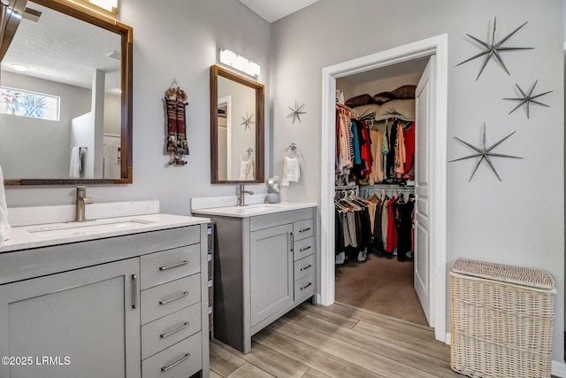 full bath featuring a sink, a walk in closet, two vanities, and wood finished floors