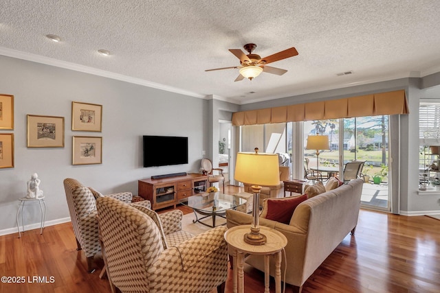 living area with a ceiling fan, wood finished floors, visible vents, baseboards, and crown molding