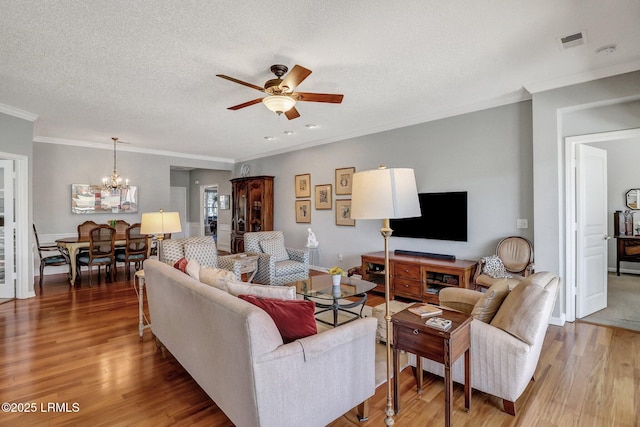 living room featuring visible vents, crown molding, light wood-type flooring, ceiling fan with notable chandelier, and a textured ceiling