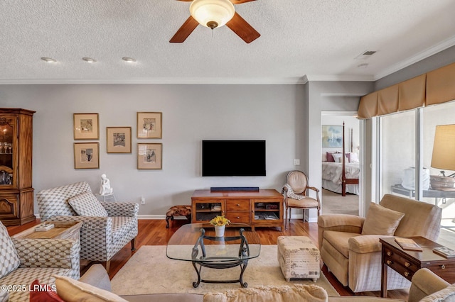 living area featuring visible vents, ornamental molding, a textured ceiling, wood finished floors, and ceiling fan