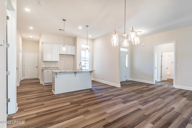 kitchen featuring decorative light fixtures, dark wood-type flooring, an island with sink, and white cabinets