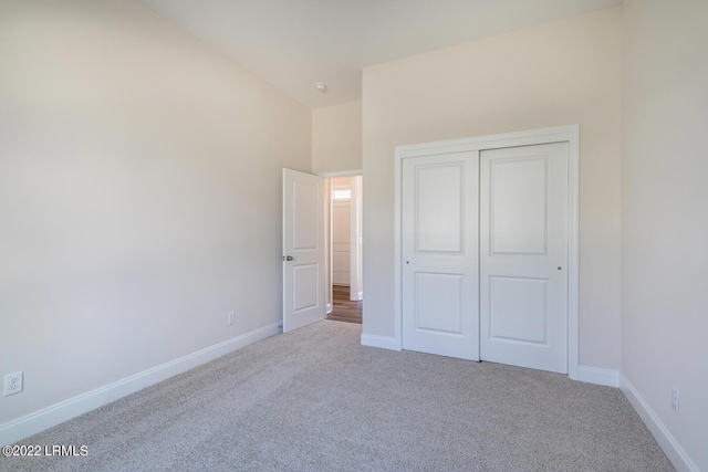 unfurnished bedroom with vaulted ceiling, light carpet, and a closet