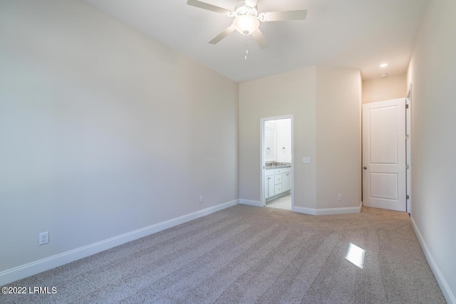 unfurnished bedroom featuring ensuite bathroom, light colored carpet, and ceiling fan