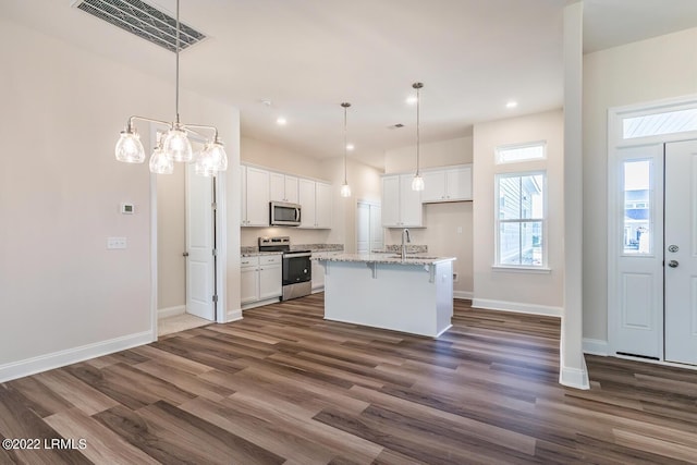 kitchen with appliances with stainless steel finishes, hanging light fixtures, an island with sink, white cabinets, and dark hardwood / wood-style flooring