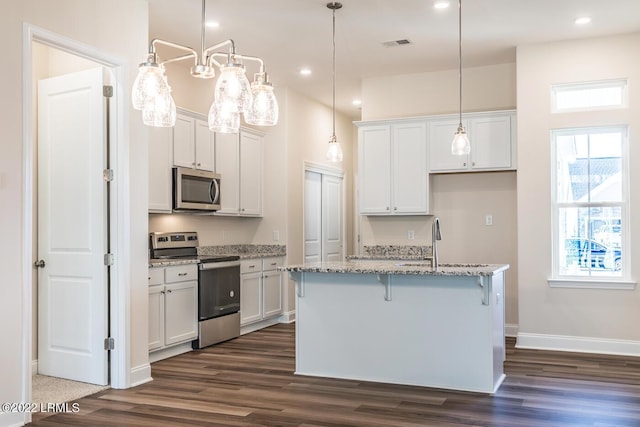 kitchen with an island with sink, white cabinets, dark hardwood / wood-style flooring, light stone counters, and stainless steel appliances