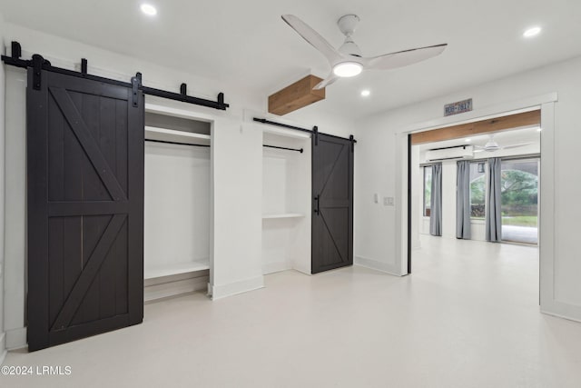 unfurnished bedroom with a barn door, ceiling fan, and a closet