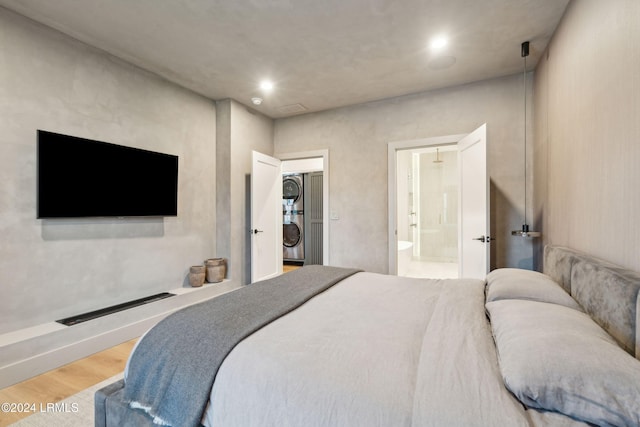 bedroom with hardwood / wood-style floors, ensuite bath, and stacked washer / drying machine