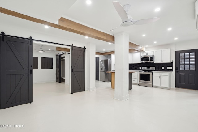 kitchen with appliances with stainless steel finishes, white cabinets, ceiling fan, a barn door, and backsplash