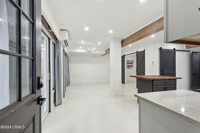 kitchen featuring gray cabinetry, a barn door, a center island, light stone countertops, and a wall unit AC