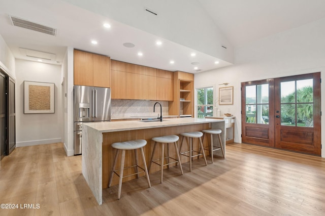 kitchen featuring sink, a breakfast bar area, a kitchen island with sink, stainless steel refrigerator with ice dispenser, and decorative backsplash