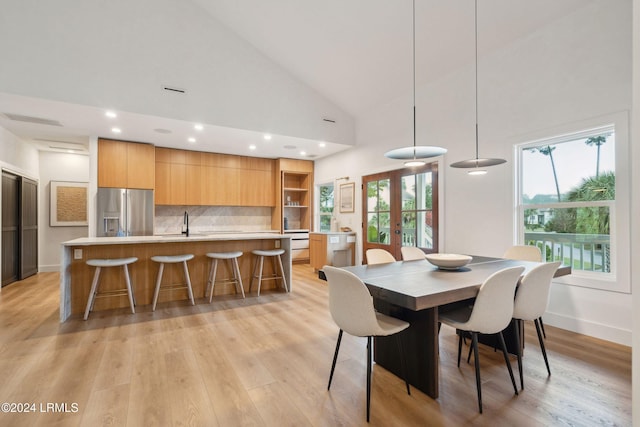 dining area with french doors, sink, high vaulted ceiling, and light wood-type flooring