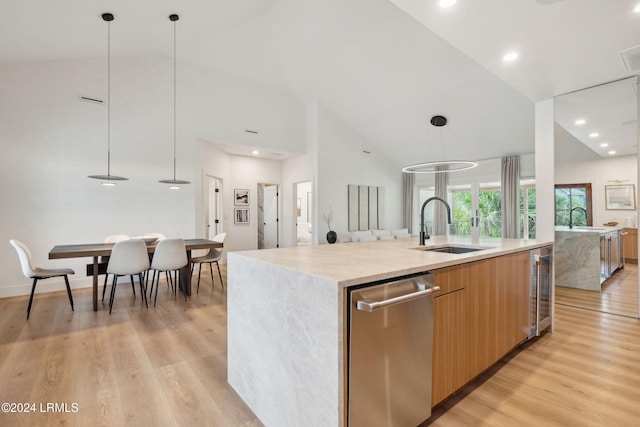 kitchen with a spacious island, sink, decorative light fixtures, stainless steel dishwasher, and light hardwood / wood-style floors