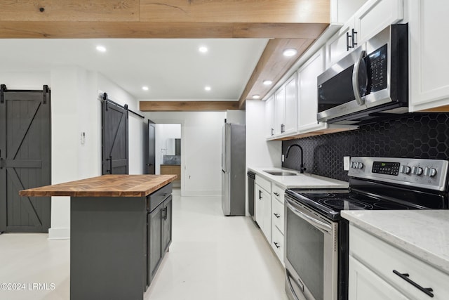 kitchen with white cabinetry, stainless steel appliances, a barn door, and wooden counters