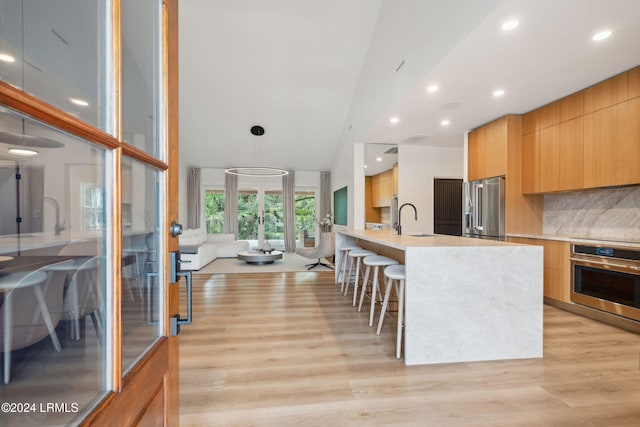 kitchen with appliances with stainless steel finishes, sink, backsplash, light hardwood / wood-style floors, and a center island with sink