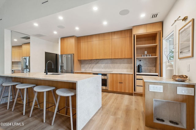 kitchen featuring sink, light hardwood / wood-style flooring, a breakfast bar, stainless steel appliances, and tasteful backsplash