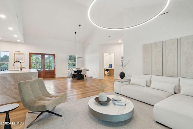 living room featuring sink, light hardwood / wood-style flooring, high vaulted ceiling, and french doors