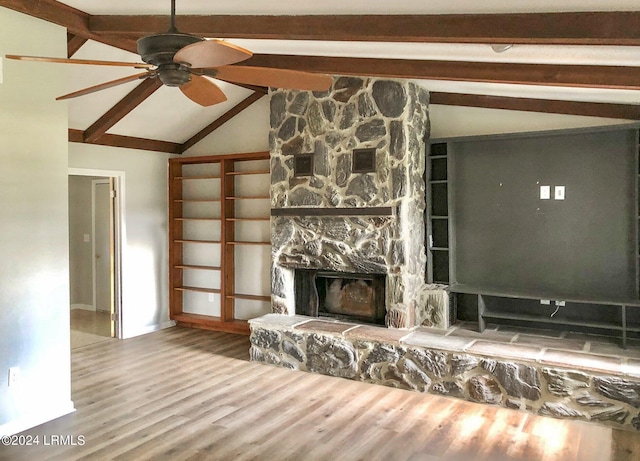 unfurnished living room featuring wood-type flooring, a stone fireplace, vaulted ceiling with beams, and ceiling fan