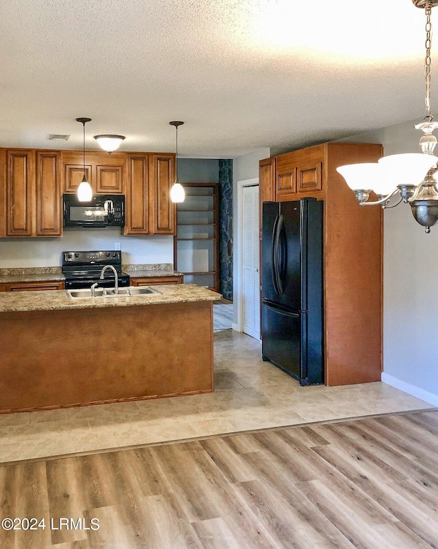 kitchen featuring sink, light wood-type flooring, hanging light fixtures, black appliances, and a textured ceiling