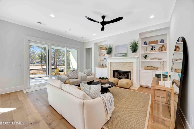 living area featuring baseboards, built in shelves, light wood-type flooring, and crown molding